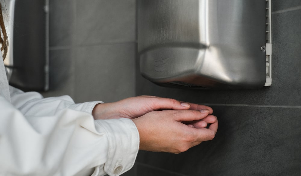 Woman in white shirt dries her hands using a commercial hand dryer in the washroom.