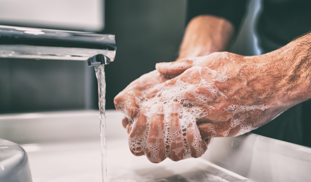 Man washing hands with soap and water in a commercial washroom. 