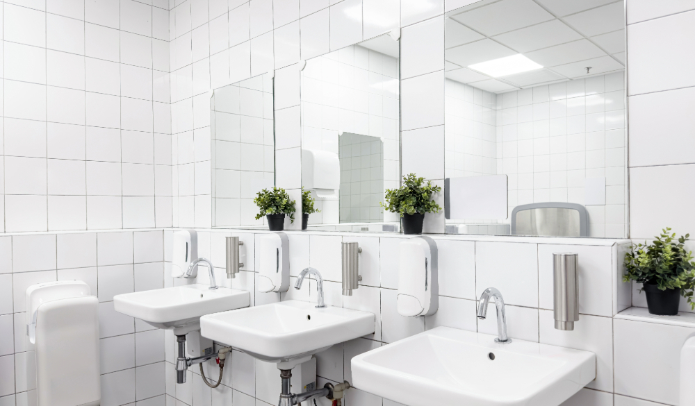 A sink with a  hand dryer and soap dispenser in a commercial washroom.