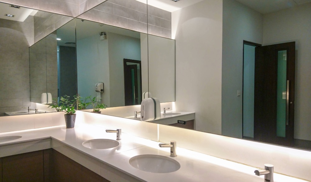 A clean and contemporary office bathroom with a large mirror and circular basins.