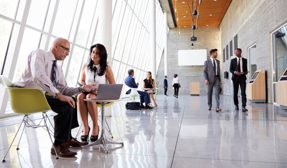 Various business meetings and conversations take place in a busy but clean office reception area.