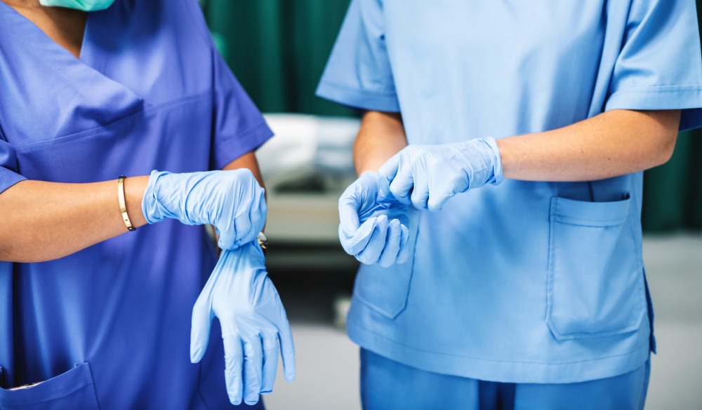 Two medical practitioners put on their blue scrubs and rubber gloves before surgery.