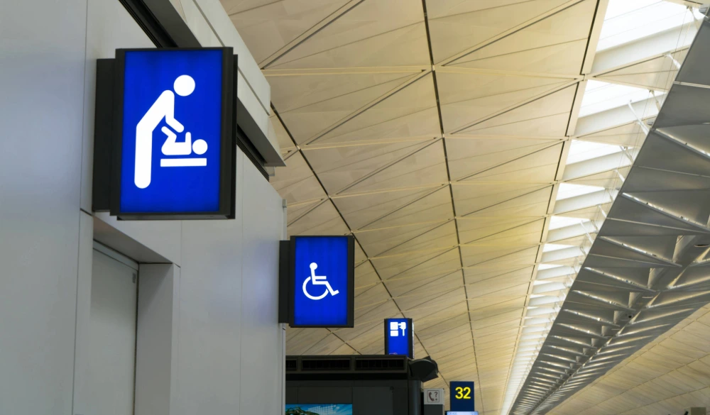 A baby changing facility sign on the wall outside of a washroom at an airport.