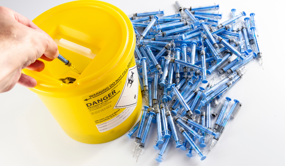 Clinical waste bin full of syringes with needles and empty vials. 