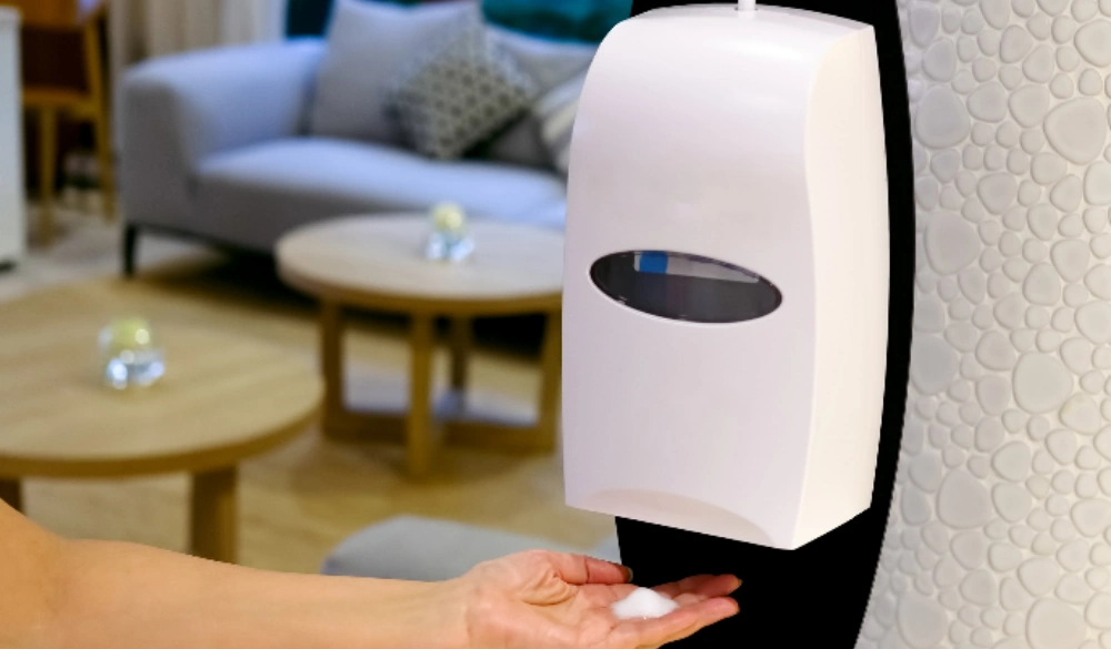 A person using a wall-mounted hand sanitiser dispenser. 