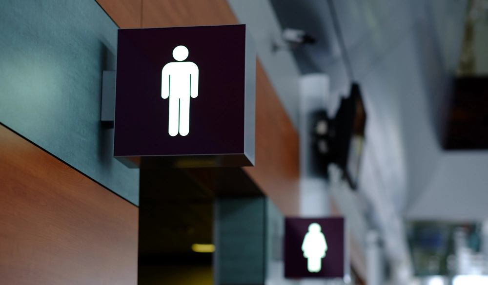 Two square signs attached to wooden wall. Both signs have lit-up figures to indicate washroom facilities. 