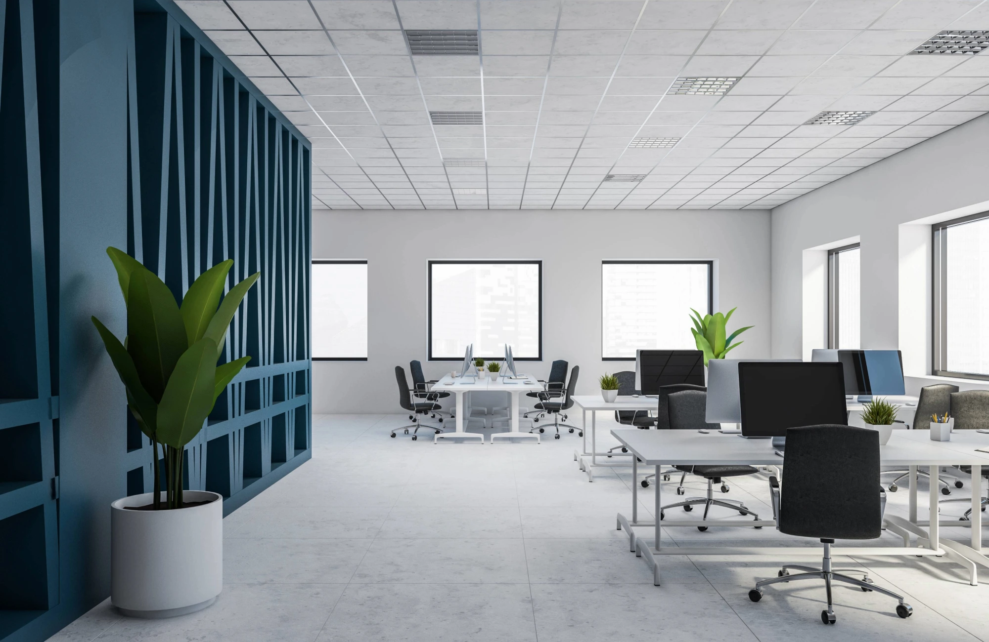 A modern, open-plan office with white walls and desks. There are several computer monitors on the desks.