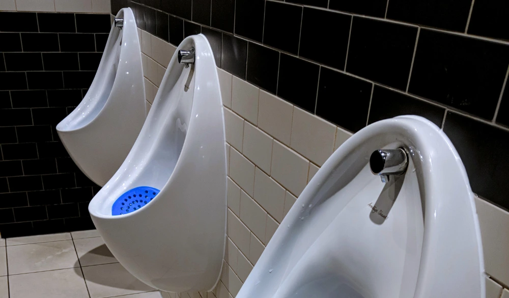 Empty male washroom with urinals with blue urinal screens.